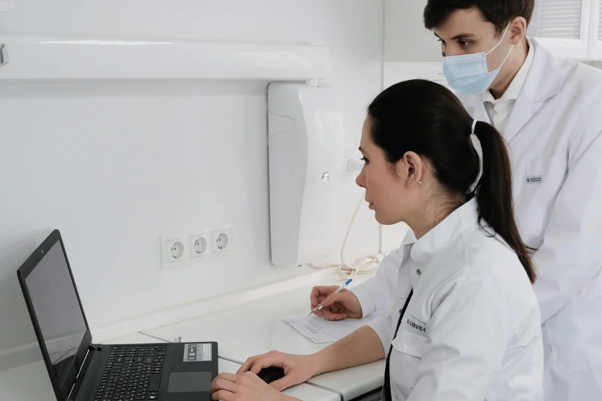 Two medical professionals in lab coats focus on a laptop. 