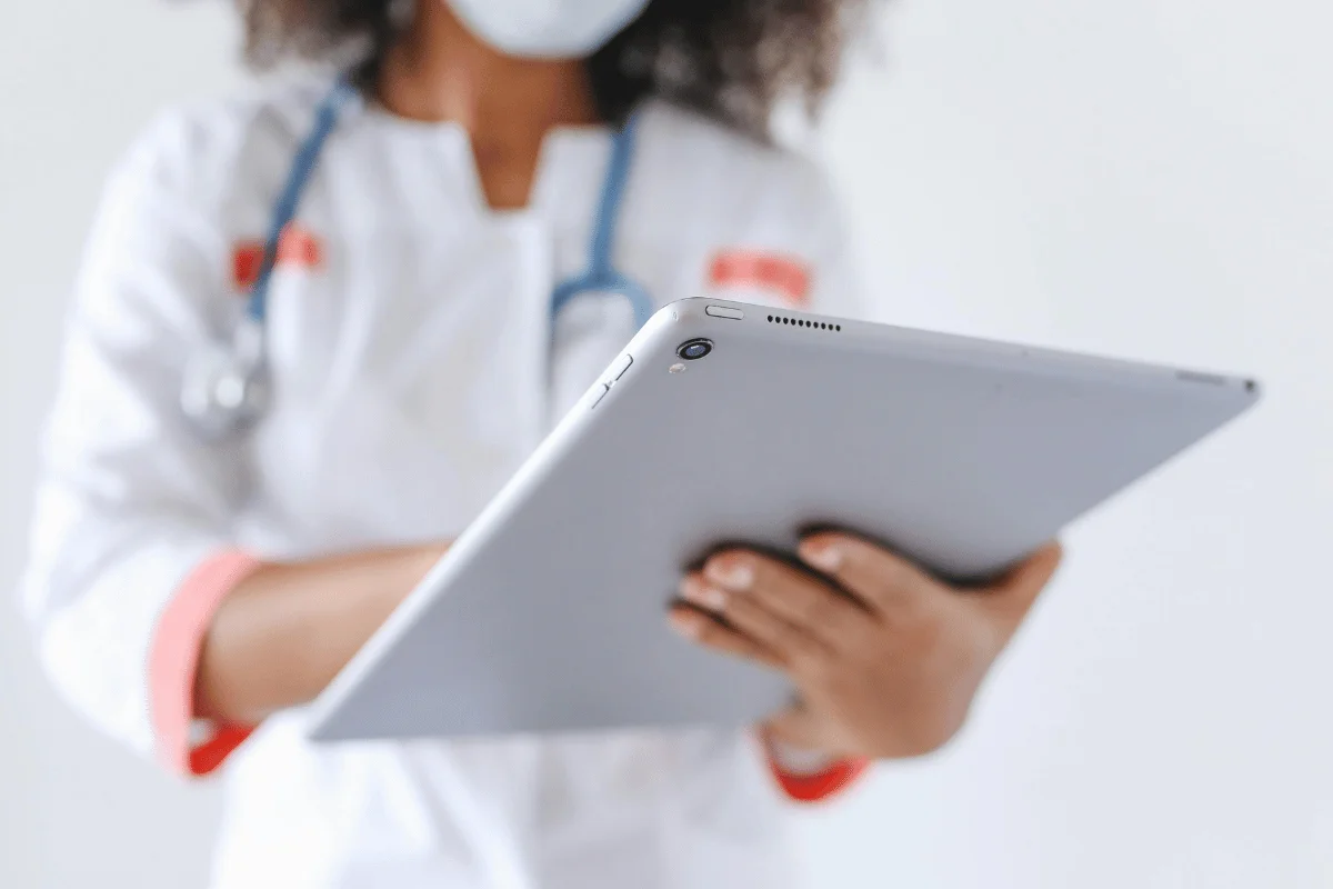 A healthcare professional in a white coat with a stethoscope holds a tablet. 