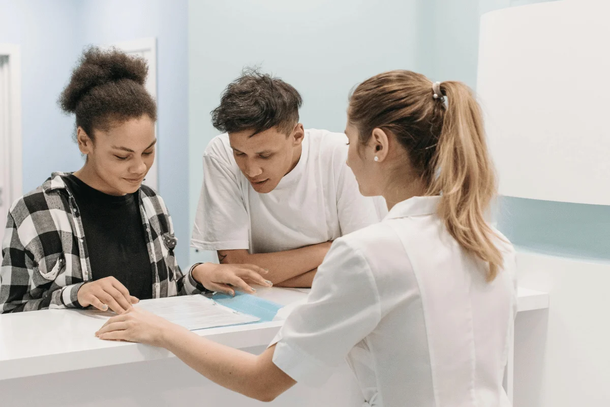 A nurse shows paperwork to a young couple at a hospital reception. 