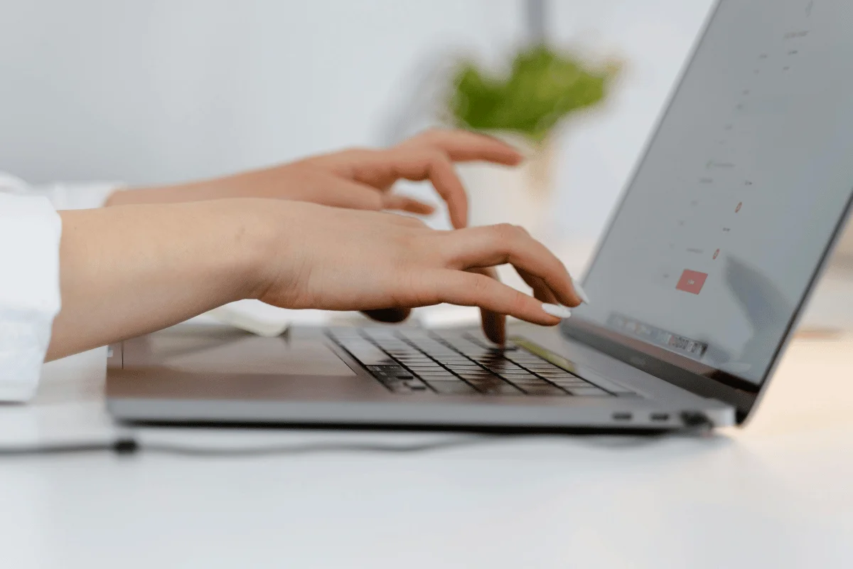 Hands typing on a silver laptop keyboard in a bright, minimalistic setting.