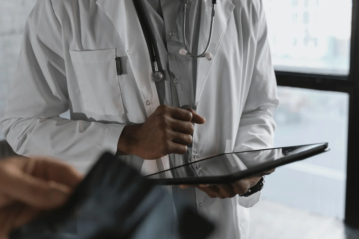 Medical professional reviewing information on a tablet while standing in a clinical setting.