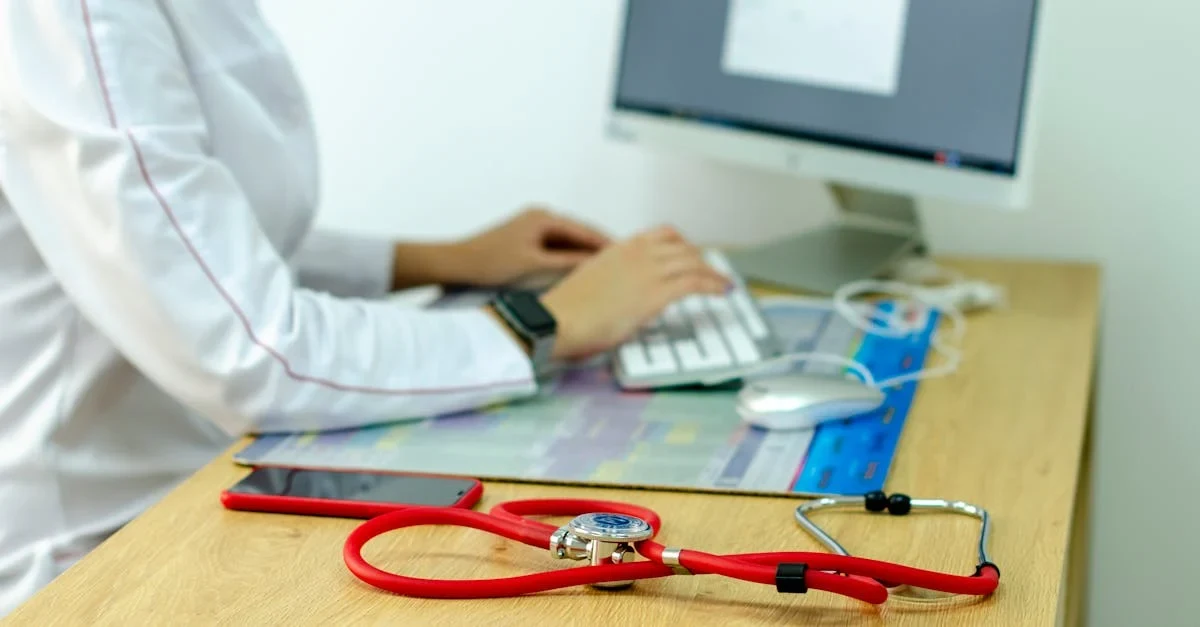 Doctor at computer workstation with red stethoscope on desk, representing autonomous medical coding technology integration.