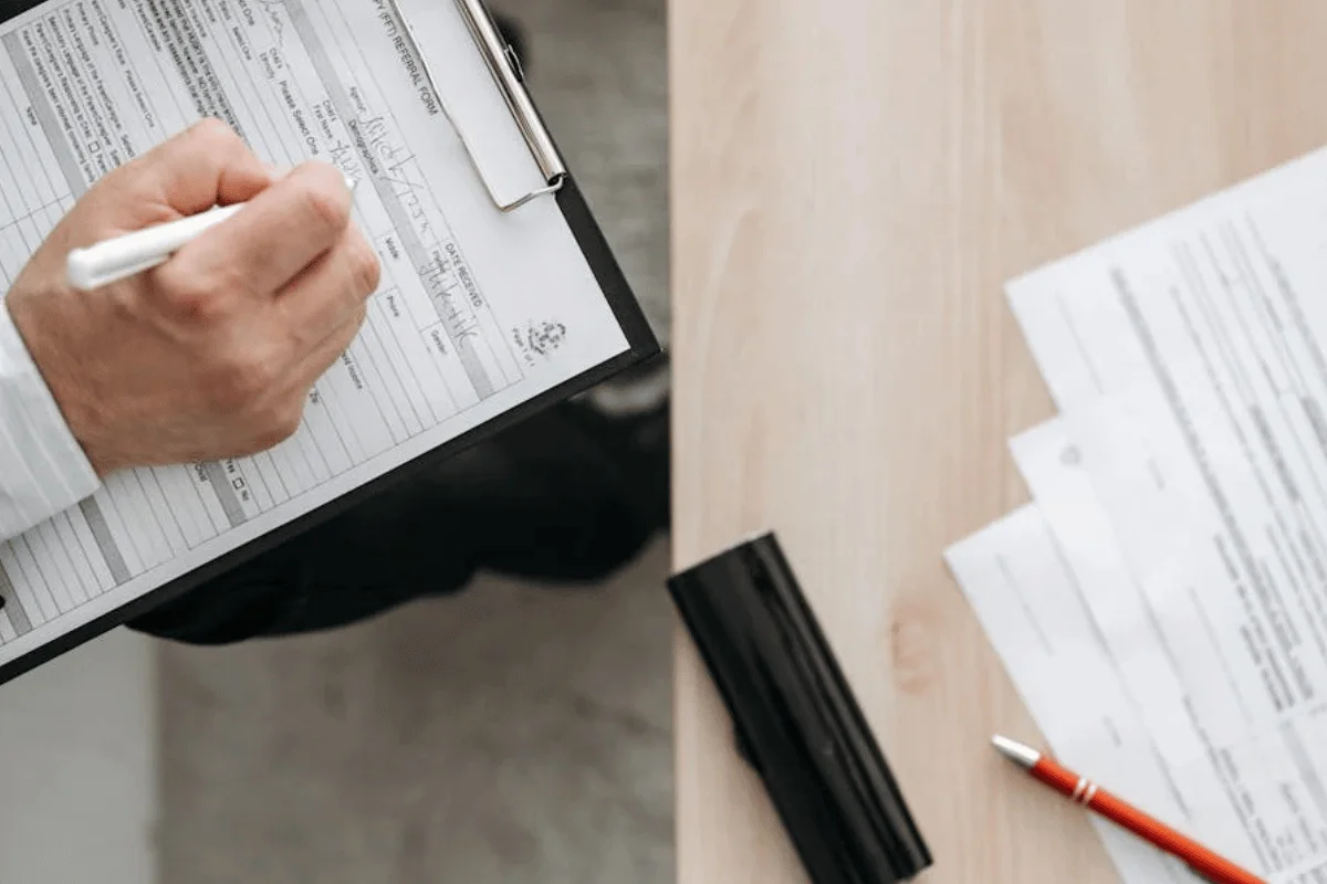 Hands completing medical coding forms on clipboards with documents spread on desk meeting productivity standards.
