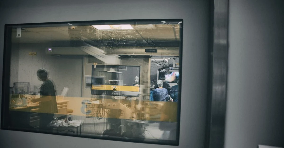Hospital observation room with staff monitoring patient through glass window, illustrating inpatient vs outpatient coding.