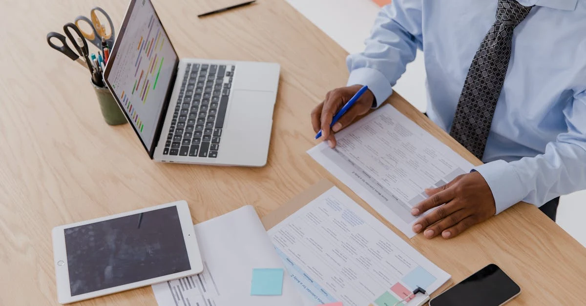 Businessman reviewing medical coding accuracy documents at desk with laptop and tablet nearby.