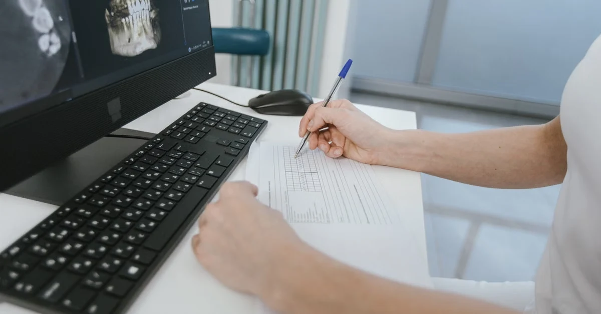 Healthcare professional manually reviewing CPT coding documentation at desk with medical imaging on computer monitor.