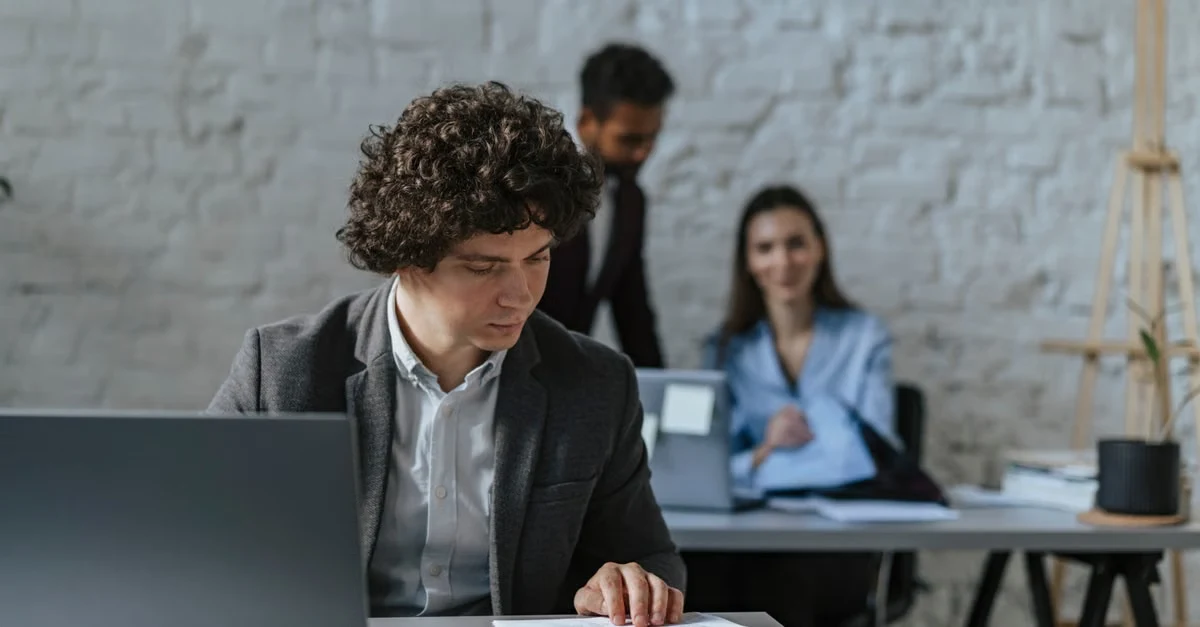 Developer working at laptop while autonomous coding vs CPT coding team collaborates in modern office background.