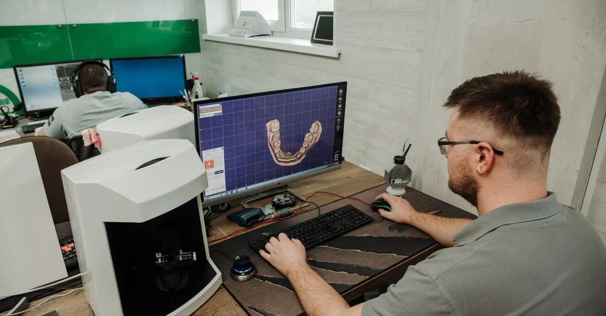 Man using inpatient medical coding software on computer monitor with 3D dental scan display in clinical workspace.
