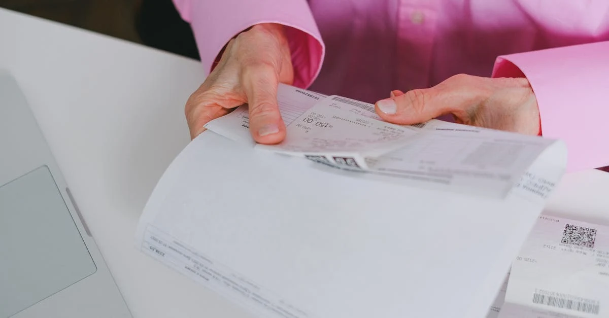 Woman in pink shirt reviewing medical billing documents and paperwork on white desk.