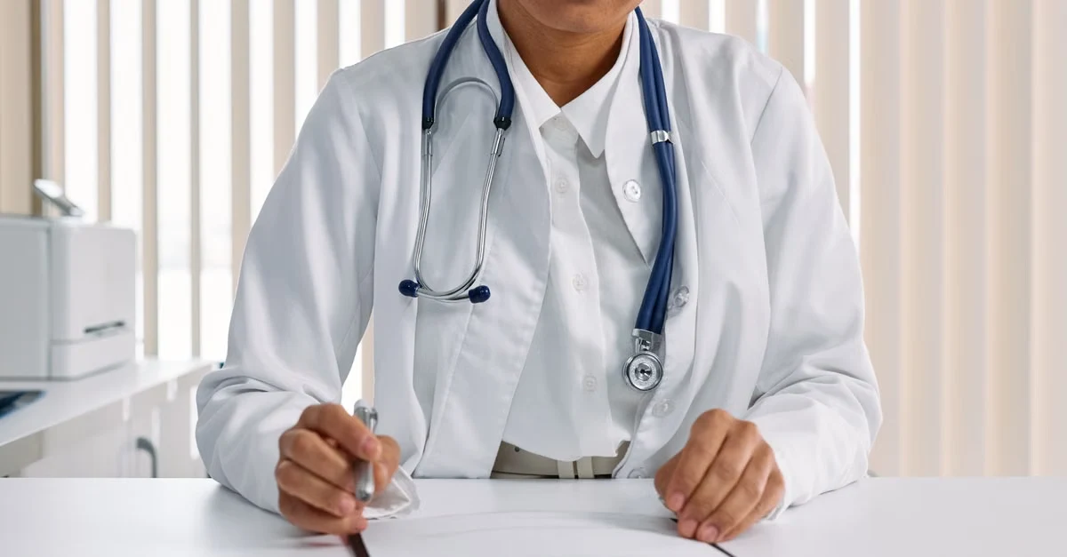 Orthopedic physician in white coat and stethoscope documenting patient notes for accurate orthopedic coding compliance.