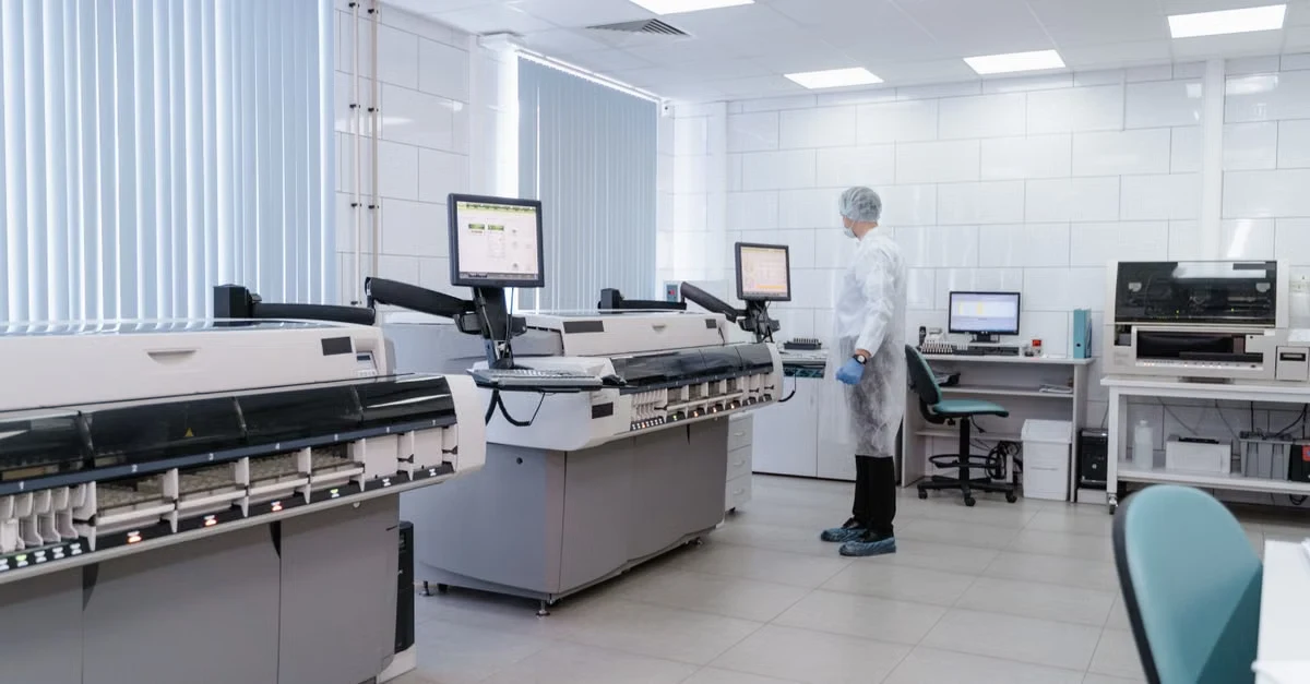Medical laboratory technician operating automated analyzer equipment in modern clinical diagnostics facility.