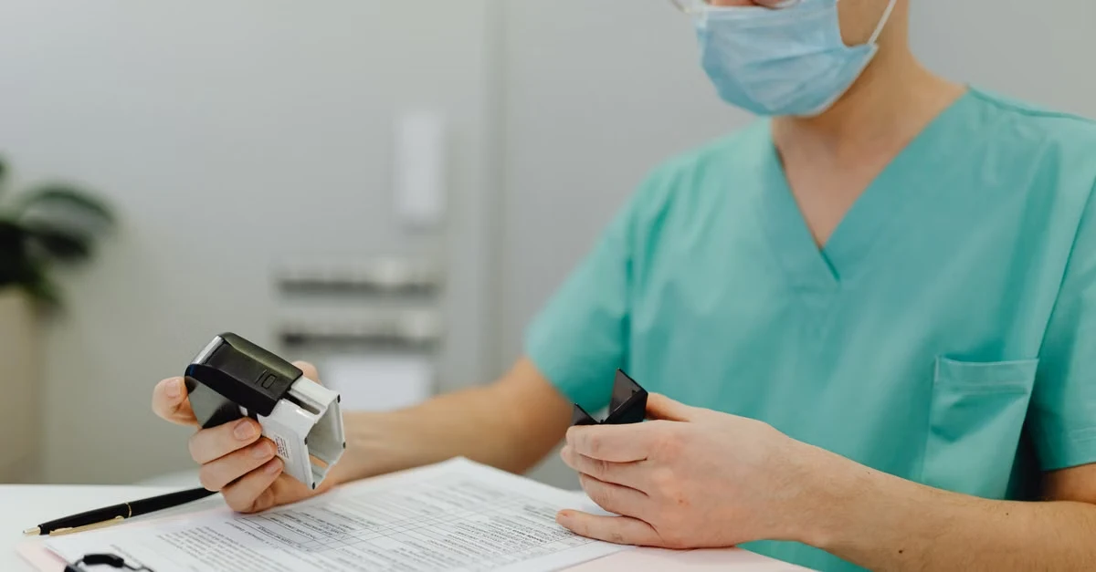 Healthcare professional in scrubs reviewing medical coding compliance documentation at desk with clipboard and stamps.