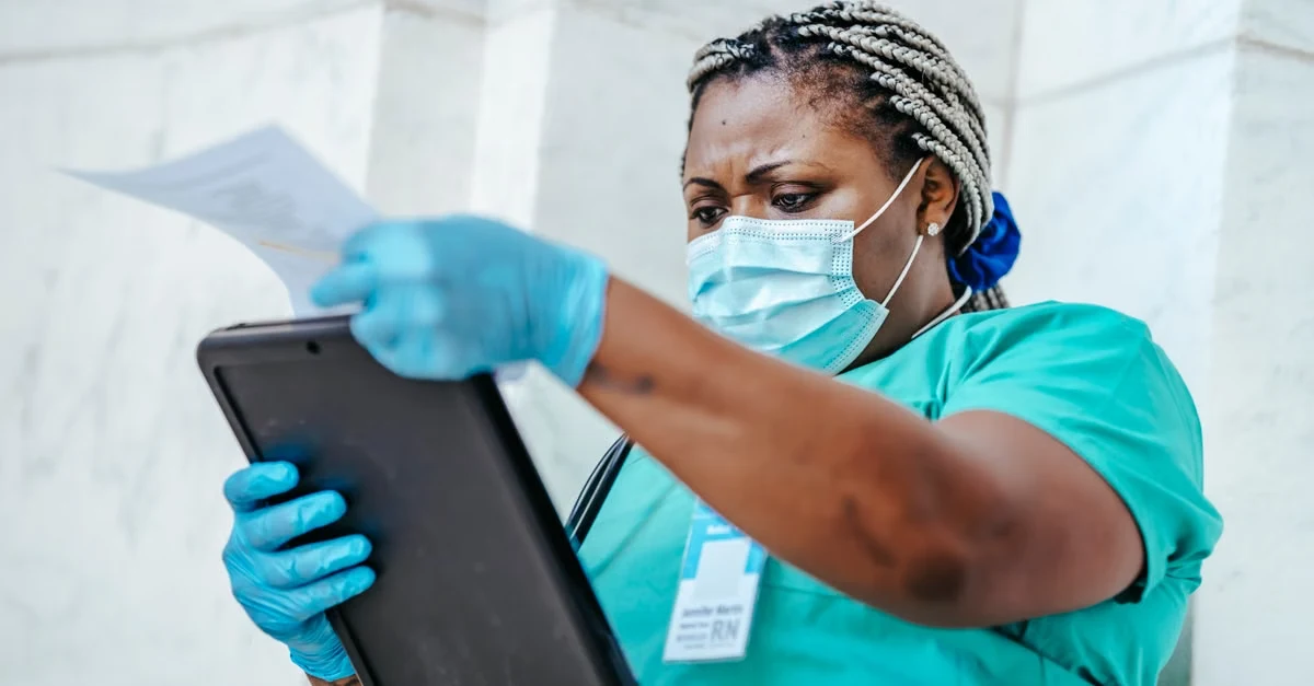 Healthcare professional reviewing spine surgery coding documentation on tablet with medical mask and gloves.