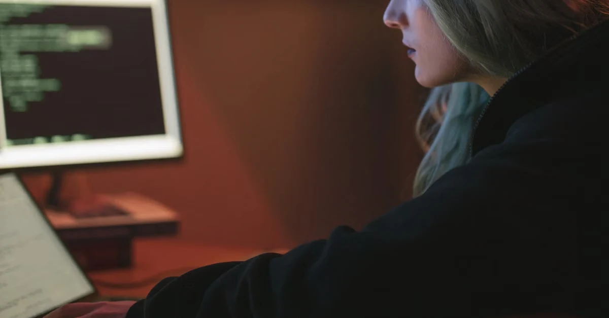 Developer reviewing spine surgery coding errors on dual monitors in dim office lighting.