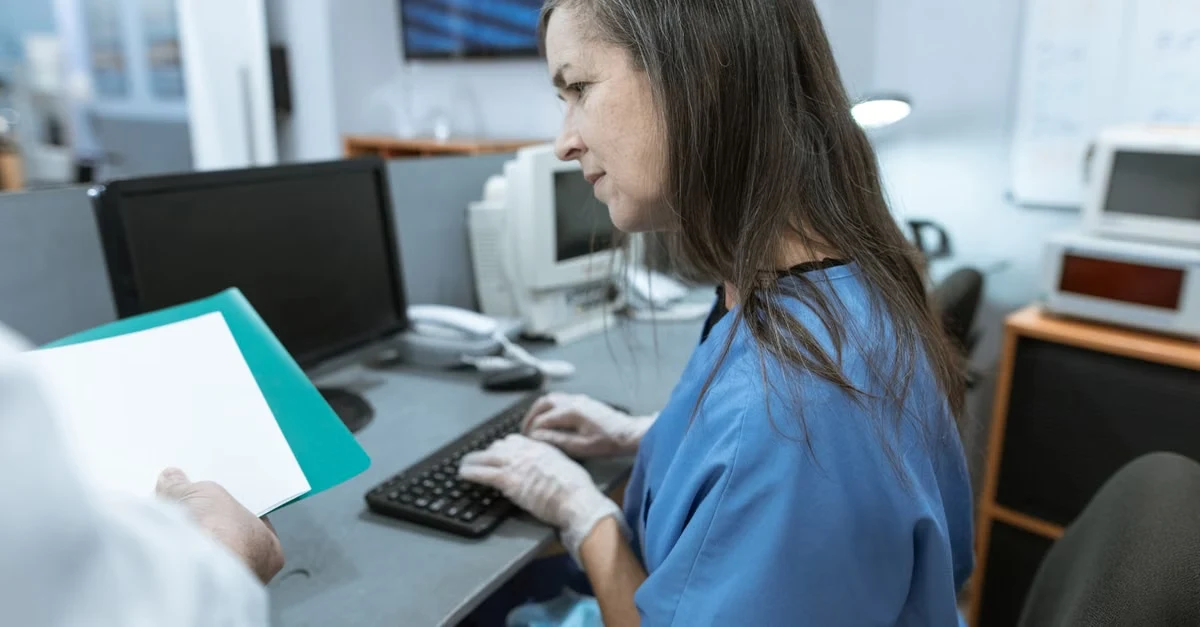 Medical coder reviewing ambulatory surgery coding guidelines at desk with computer and documents.