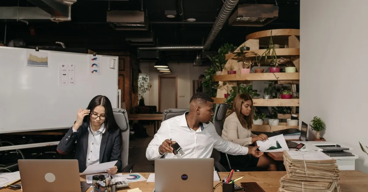 Diverse team collaborating at wooden desk with laptops, notebooks, and medical billing calculator tools in modern office..
