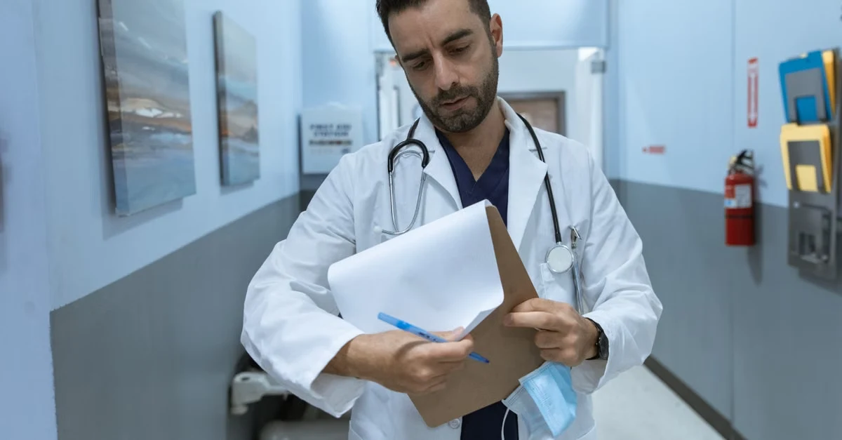 Doctor in white coat reviewing patient charts in hospital hallway for reducing hospital readmissions analysis.