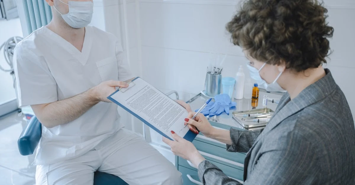 Healthcare provider showing patient clipboard with medical form in clinical setting.