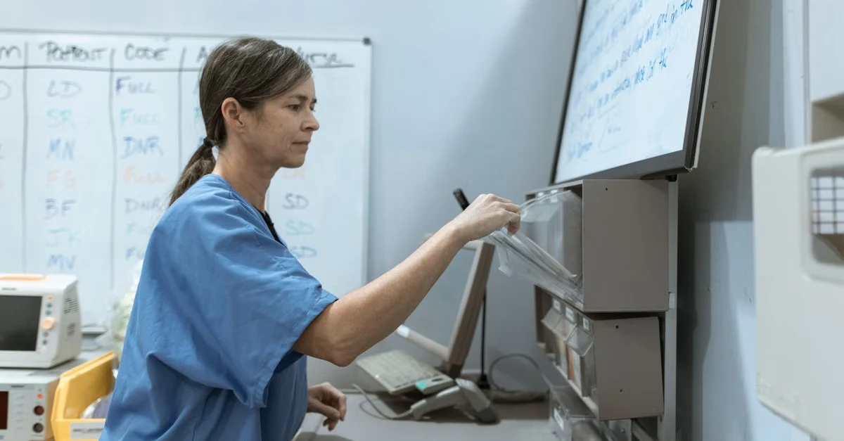 Healthcare professional writing notes on medical equipment screen during patient workflow documentation process.