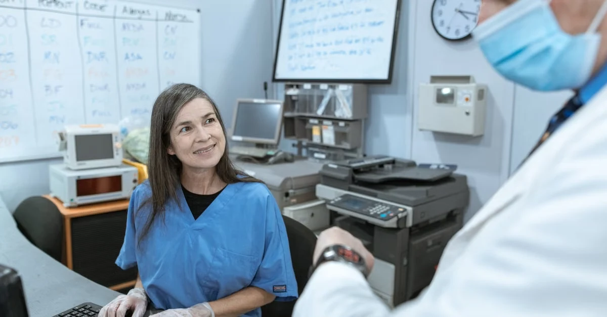 Healthcare worker at computer discussing revenue cycle management automation workflow in clinical office setting.