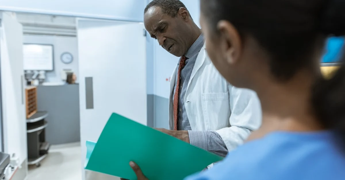 Doctor reviewing green medical coding risk adjustment documentation with colleague in clinical laboratory setting.