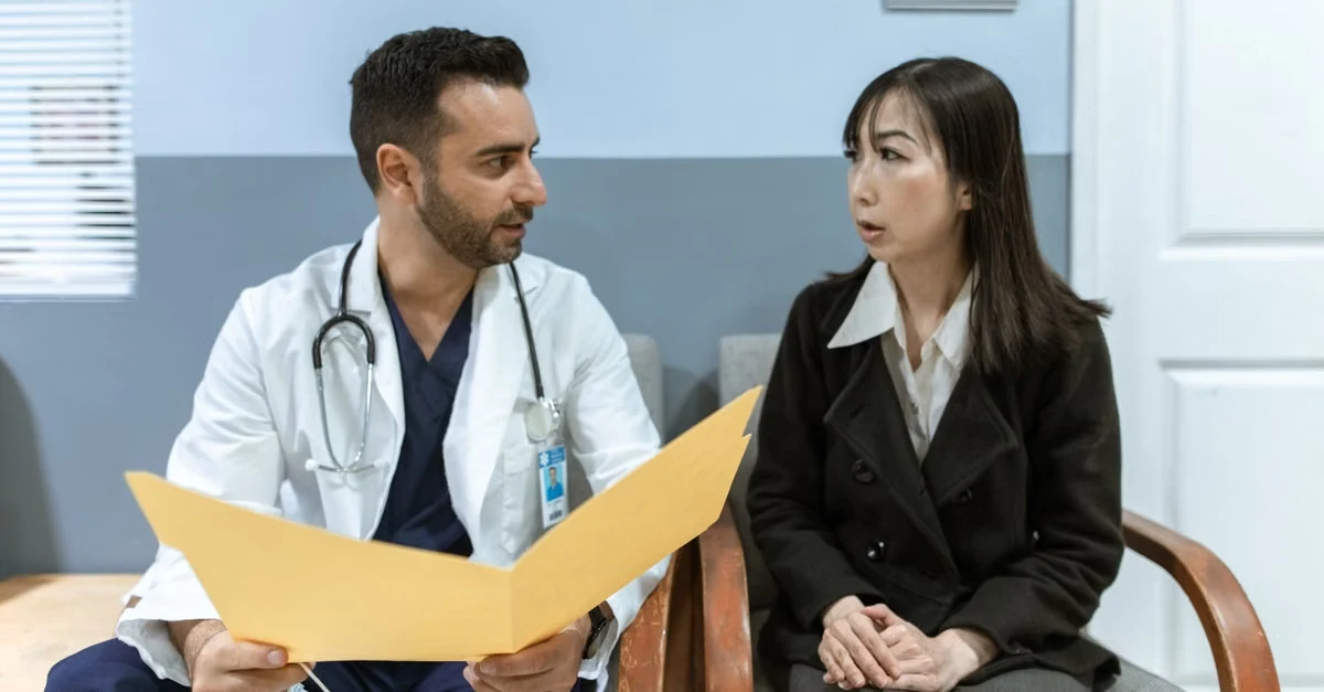 Male doctor reviewing patient records with female patient during medical consultation in clinical office setting.