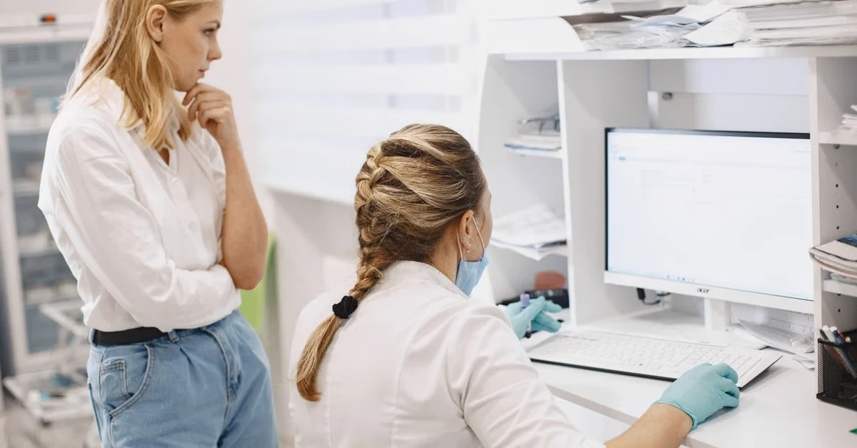 Two healthcare professionals discussing medical coding risk adjustment data at laboratory workstation with equipment.