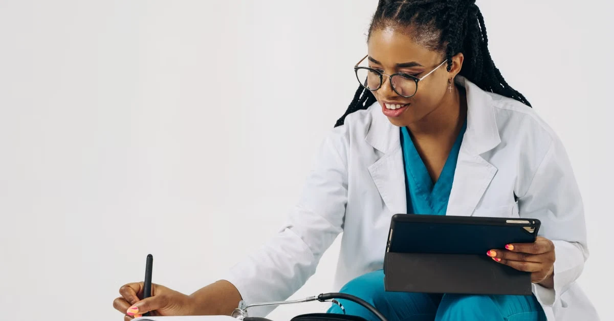 Doctor in white coat using tablet while writing notes, comparing sully vs abridge healthcare documentation tools.