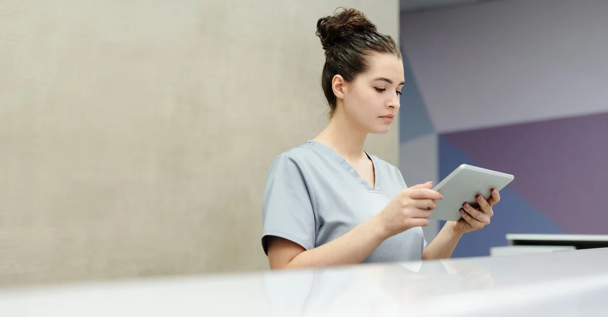 Healthcare worker reviewing patient data on tablet at reception desk.