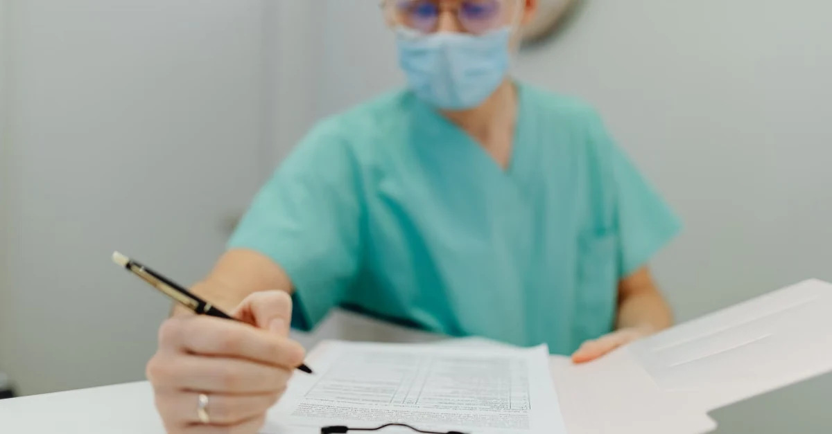 Healthcare professional in scrubs and mask completing patient documentation, representing healthcare charge capture.