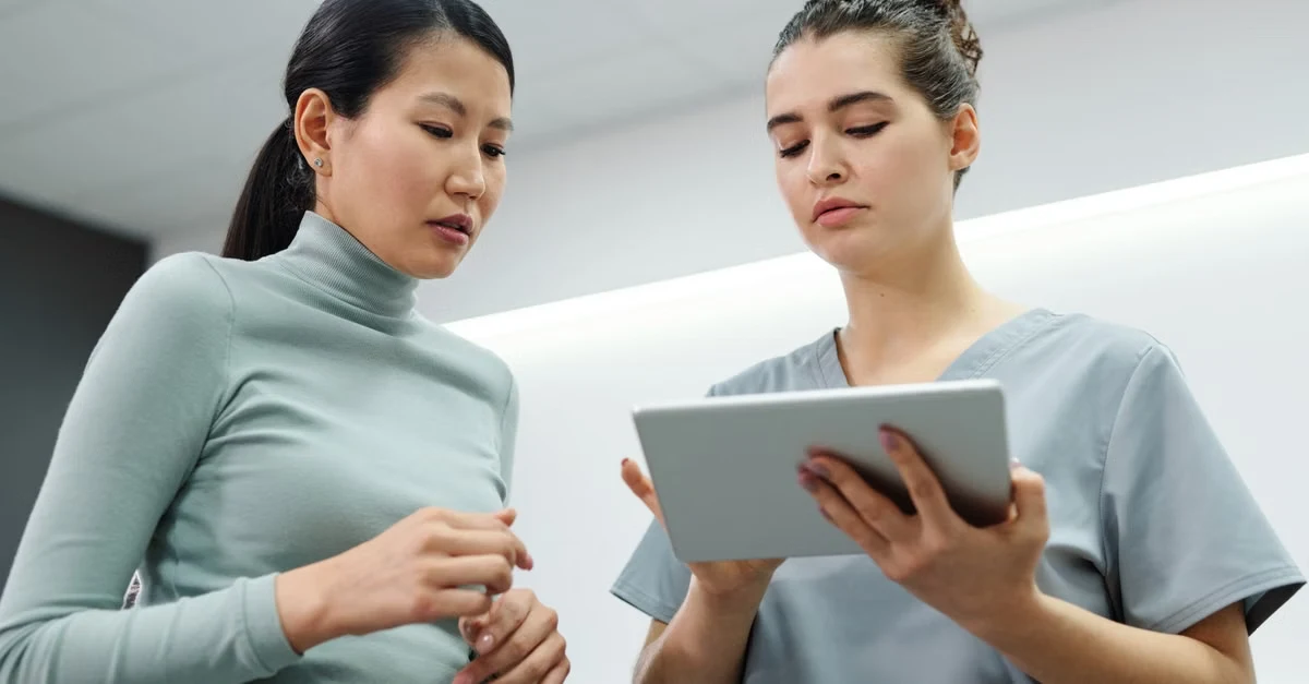 Healthcare professional and patient review healthcare revenue cycle management information on tablet together indoors.