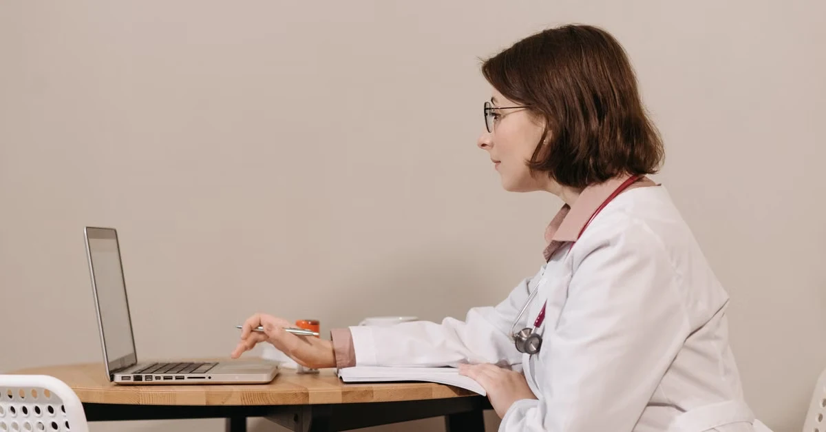 Female physician working at desk with laptop, illustrating physician burnout rates specialty concerns in healthcare.