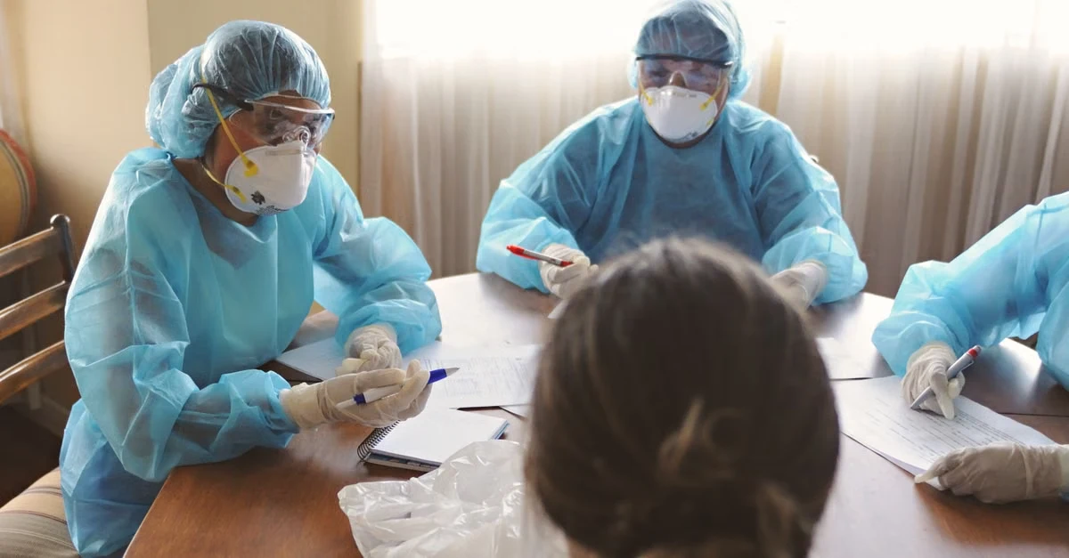 Healthcare professionals in protective gear conducting clinical workflow assessment during patient consultation meeting.