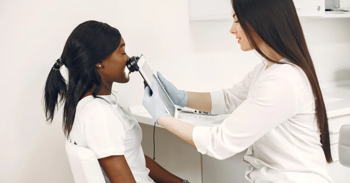 Dermatologist using AI scribe technology during skin examination with patient in clinical setting.