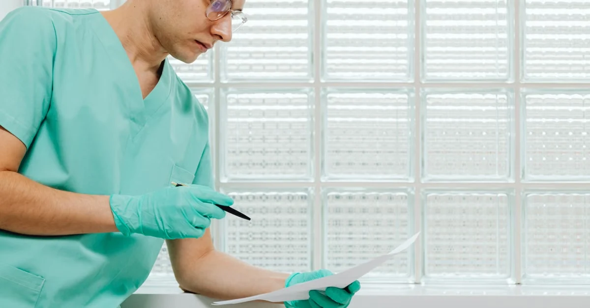 Doctor in scrubs reviewing AI soap notes on tablet near window with frosted glass background.