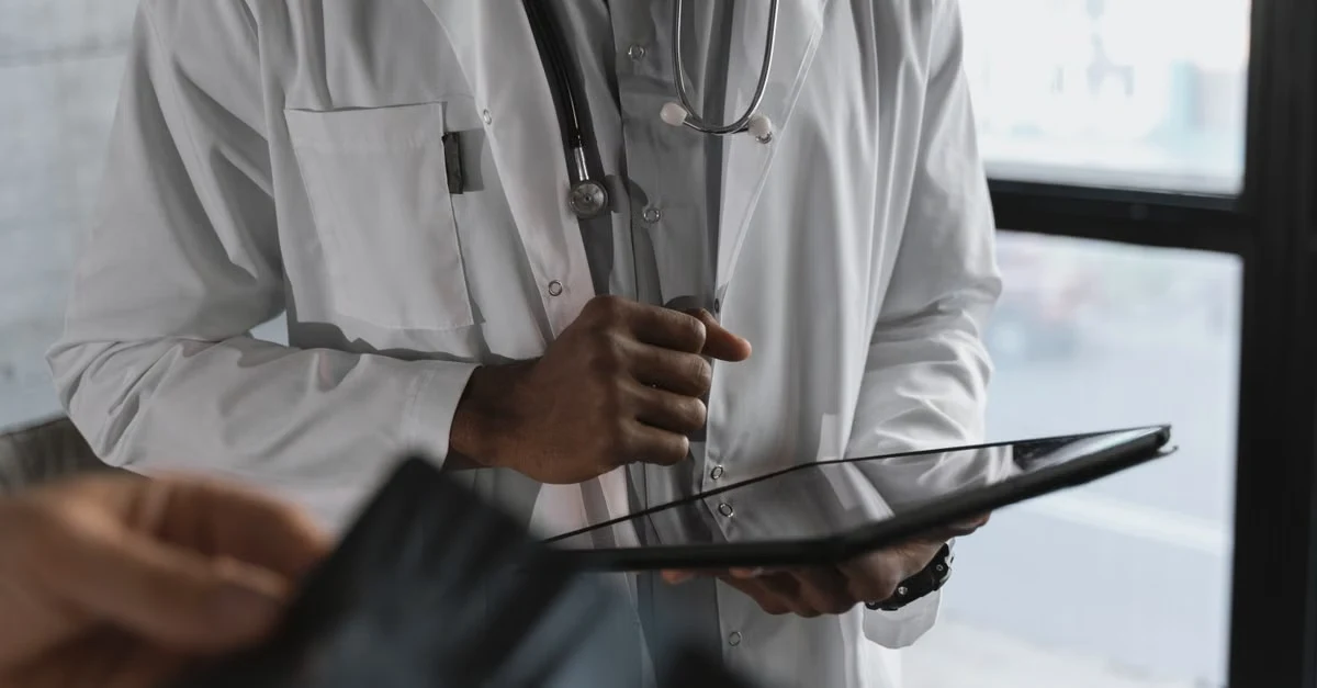 Psychiatrist holding tablet with stethoscope, reviewing AI scribe psychiatry documentation in clinical setting.