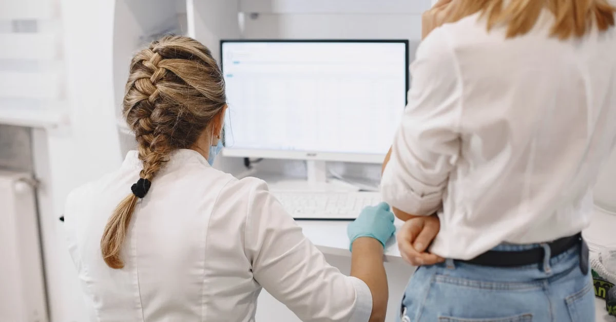 Two healthcare professionals reviewing patient data on monitor in family medicine clinic office setting.