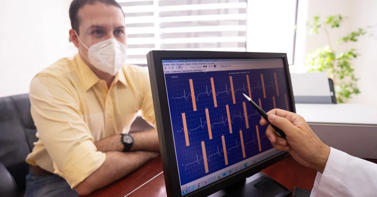 Healthcare professional in mask reviewing cardiac waveform data on tablet with AI scribe cardiology analysis software.