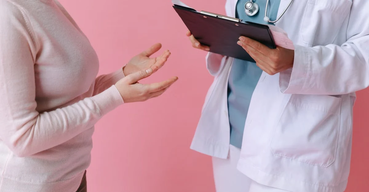 Doctor with tablet consulting patient about gynecology AI scribe documentation against pink background.
