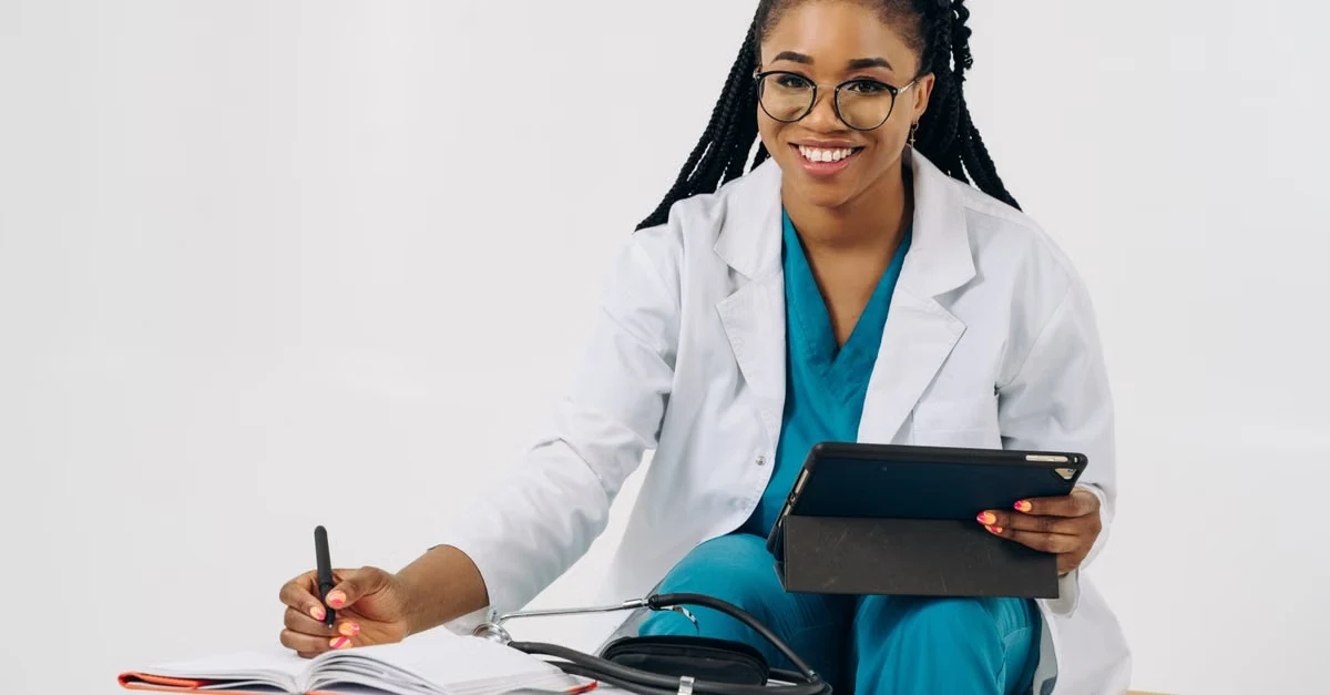 Female gynecologist in white coat writing notes while holding tablet, demonstrating gynecology AI scribe workflow efficiency.