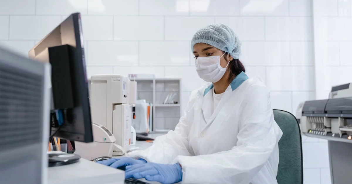 Healthcare worker in surgical attire at computer workstation ensuring medical coding compliance in laboratory setting.