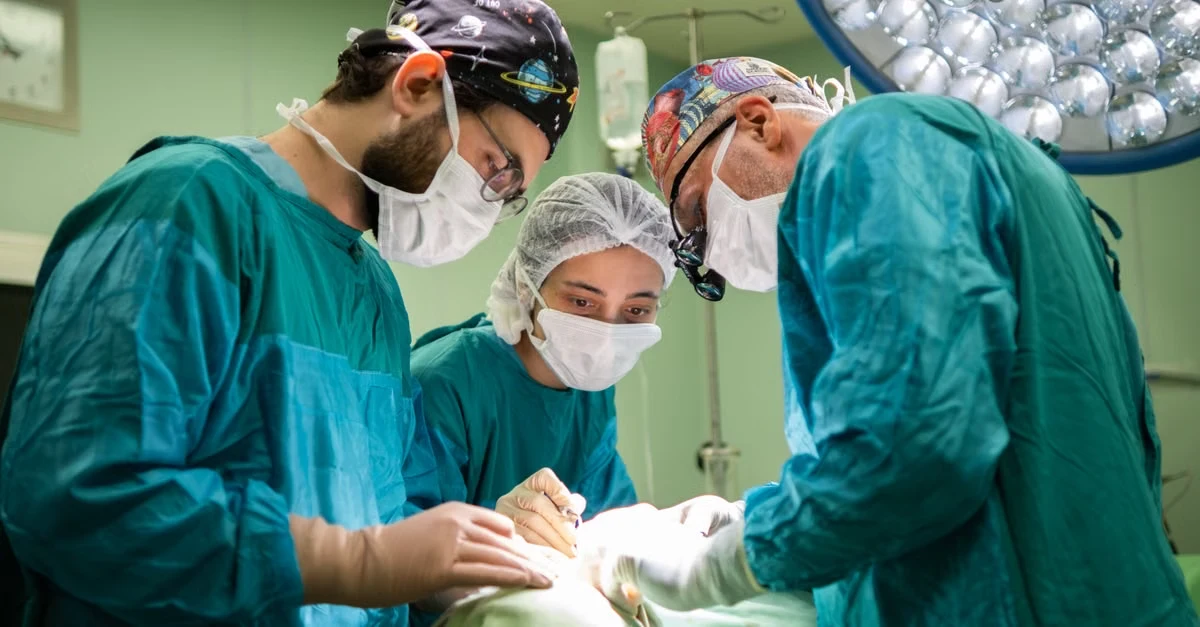 Surgical team performing general surgery procedure in operating room with overhead lighting and instruments.