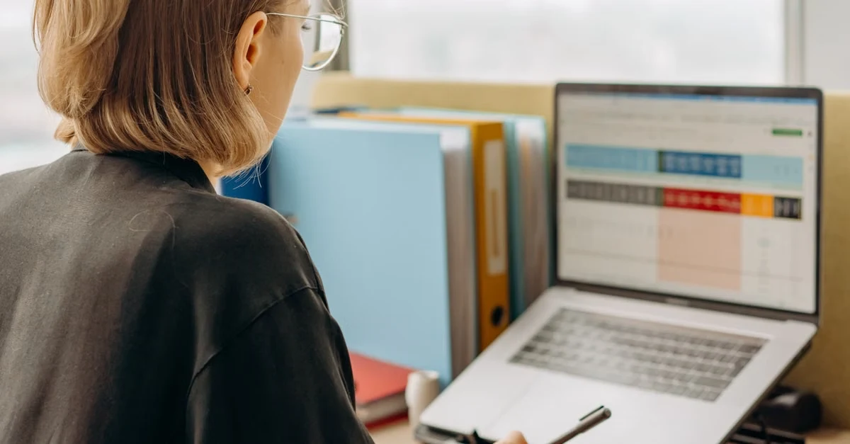 Woman reviewing medical coding risk adjustment data on laptop screen with color-coded documentation and reference materials.
