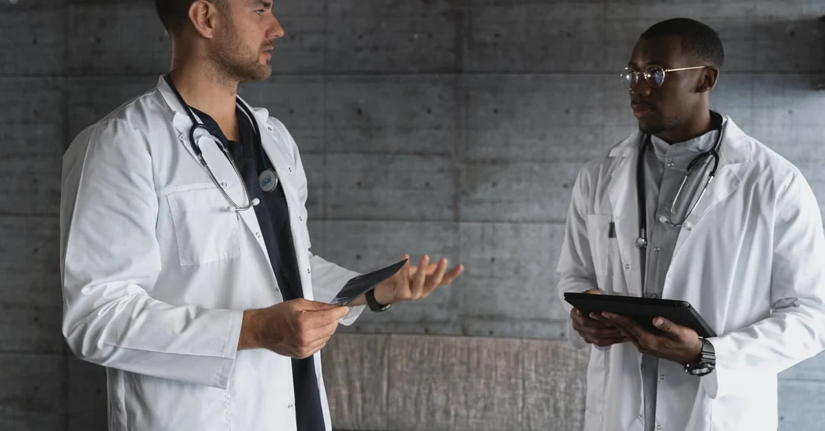 Two doctors in white coats discussing autonomous medical coding challenges while holding tablets in modern hospital setting.